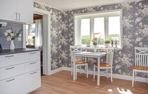 Eine Küche mit weißen Schränken, einem Esstisch mit Stühlen, einem Fenster mit Vorhängen und floralem Wandpapier.