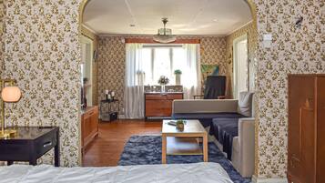 Une pièce comprenant un lit, un canapé, une petite table, une armoire, un miroir, une fenêtre et un lustre.