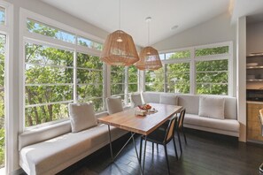 A sunlit room with a wooden table, two chairs, a cushioned bench, and large windows. - Sunlit Updated Victorian - Chef`s kitchen, library and sunroom, Boston 20 min by car or train (Melrose)