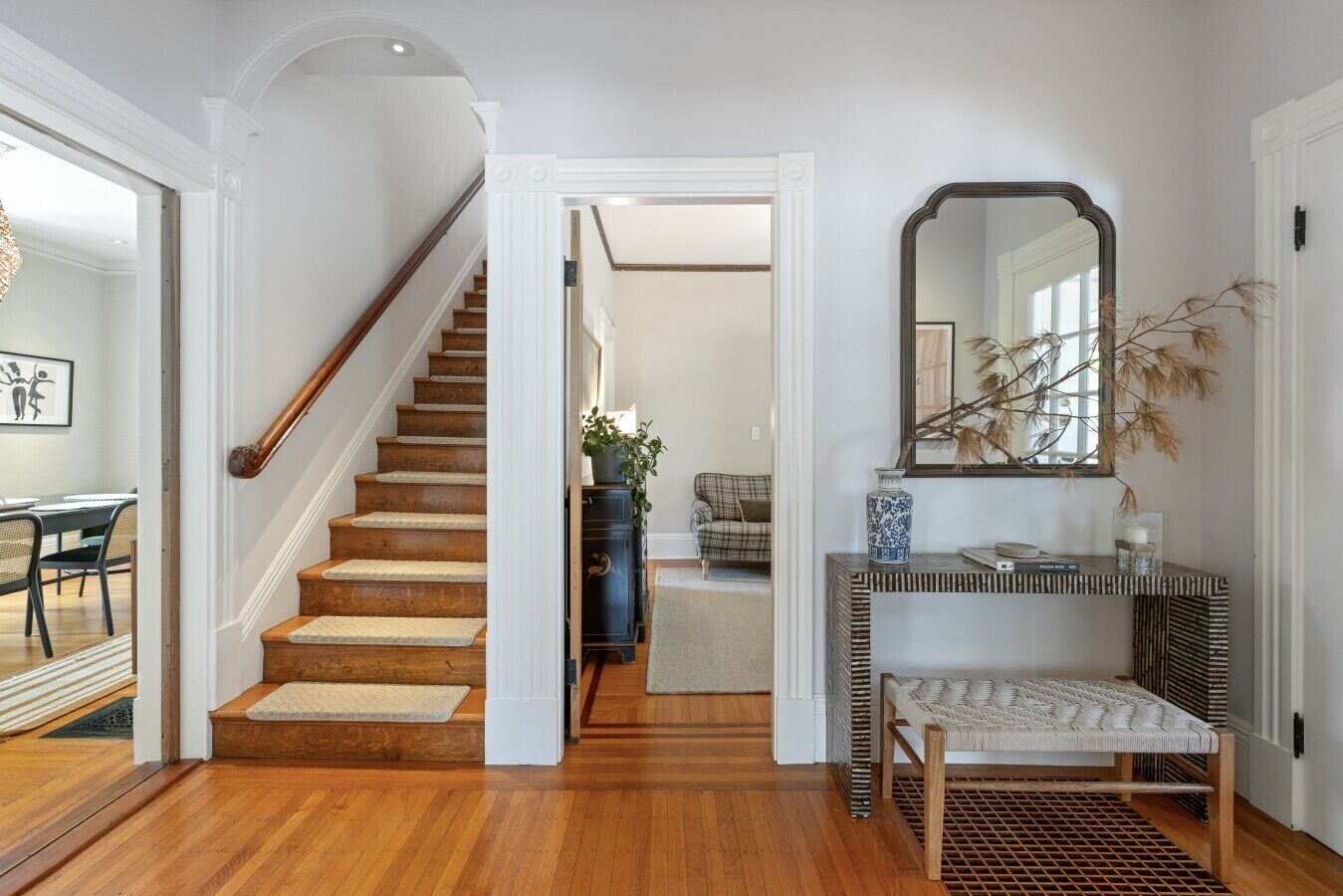 Un escalier mène à un espace de vie comprenant un canapé, une console ornée d’objets décoratifs et un miroir accroché au mur.