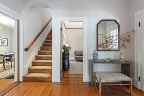 A staircase leading to a living area with a sofa, a console table with decorative items, and a mirror on the wall. - Sunlit Updated Victorian - Chef`s kitchen, library and sunroom, Boston 20 min by car or train (Melrose)