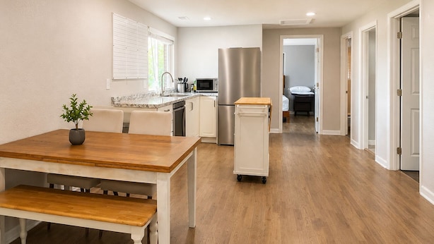 A modern kitchen with a dining area, wooden flooring, and a refrigerator. - 1,100 sf Spacious Cozy 2BR Near Denver DT, Red Rocks, and Rockies! (Arvada)