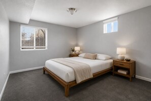 Un dormitorio con cama, mesitas de noche, lámpara de techo y ventana con persianas.