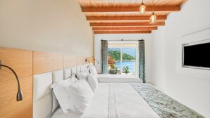 A bedroom with a bed, wooden headboard, a TV, and a view of a balcony with a scenic landscape.