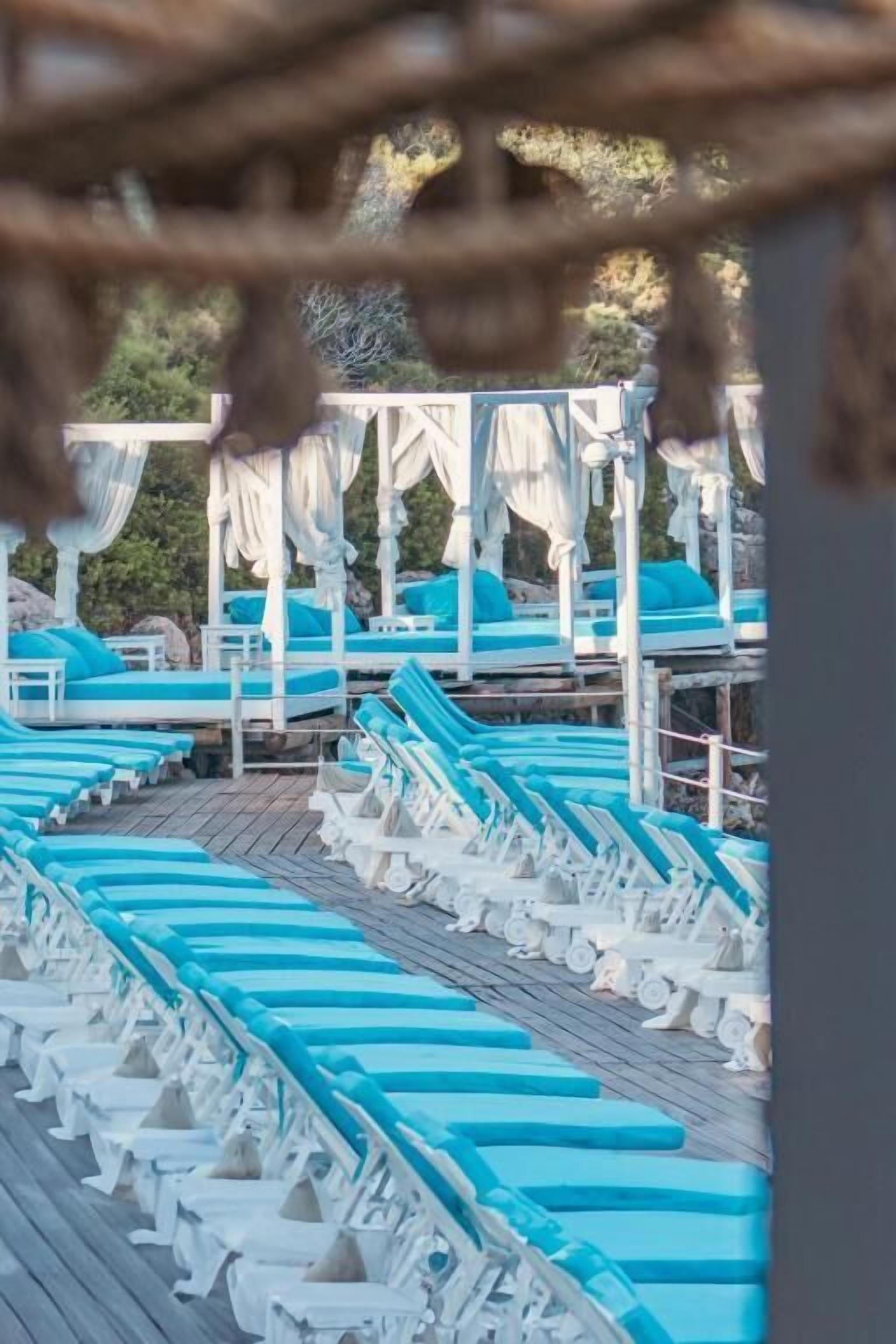 Een rij witte lounge fauteuils met blauwe kussens, op een houten terras.