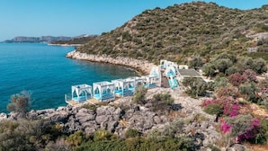 A coastal hotel with a series of white structures with blue accents, situated on a rocky terrain with a view of the sea.