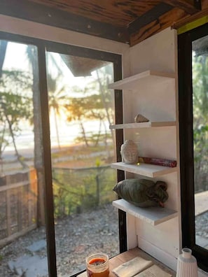 Ein Zimmer mit Fenster, einem Regal mit Buddha-Statue, einem Kissen, einem Krug und einer kleinen Vase.