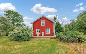 Ein rot gehaltenes, stallähnliches Haus mit Veranda, umgeben von üppigem Grün und Bäumen.