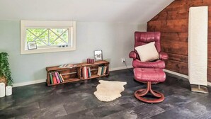 A room with a dark wooden floor, a red leather chair with a cushion, a bookshelf, a window with a view, and a white rug. - 2 bedroom lovely home in Lönashult (Lönashult)