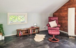 A room with a dark wooden floor, a red leather chair with a cushion, a bookshelf, a window with a view, and a white rug. - 2 bedroom lovely home in Lönashult (Lönashult)