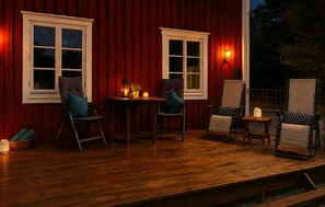 Une terrasse en bois avec deux tables et quatre chaises, une lanterne et une bougie posée sur le sol.