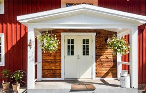 A red barn with a white door, wooden siding, and hanging flower baskets. - 2 bedroom cozy home in Lönashult (Lönashult)