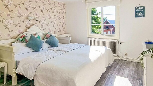 A bedroom with a bed, bedside tables, a radiator, a window, and a view of a house outside. - 2 bedroom lovely home in Lönashult (Lönashult)