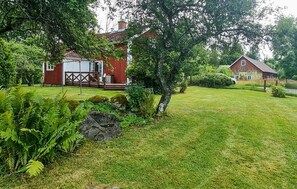 A red barn with a white door, surrounded by a grassy yard with ferns and a large tree. - 2 bedroom lovely home in Lönashult (Lönashult)