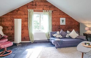 A cozy room with a sloped ceiling, a window with curtains, a sofa with cushions, a small table, and a chair. - 2 bedroom lovely home in Lönashult (Lönashult)