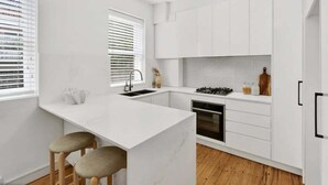 Una cocina moderna con armarios blancos, encimera de mármol, cocina a gas y suelo de madera.