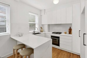 Eine moderne Küche mit weißen Schränken, einer Marmorarbeitsplatte, einem Gasherd und Holzboden.