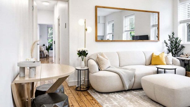 Una sala de estar moderna con sofá, reposapiés, mesa de centro redonda y una mesita auxiliar con lámpara.