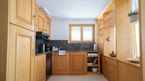A compact kitchen with wooden cabinets, a built-in oven, and a window with blinds. - Via Radiras - Laax | Flims | Lake Cauma | Hiking (Laax)