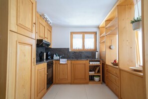 A compact kitchen with wooden cabinets, a built-in oven, and a window with blinds. - Via Radiras - Laax | Flims | Lake Cauma | Hiking (Laax)