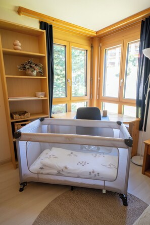 A room with a crib, wooden shelves, a desk, and large windows. - Via Radiras - Laax | Flims | Lake Cauma | Hiking (Laax)