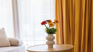 A round wooden table with a white vase containing flowers, positioned on a textured rug in a room with a sofa and curtains. - Via Radiras - Laax | Flims | Lake Cauma | Hiking (Laax)