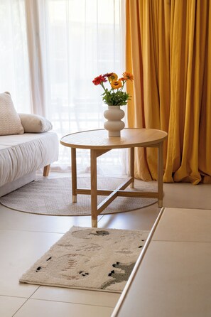 A round wooden table with a white vase containing flowers, positioned on a textured rug in a room with a sofa and curtains. - Via Radiras - Laax | Flims | Lake Cauma | Hiking (Laax)