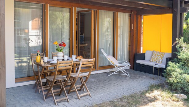 An outdoor patio with a wooden table set for dining, a lounge chair, and a sofa with cushions. - Via Radiras - Laax | Flims | Lake Cauma | Hiking (Laax)