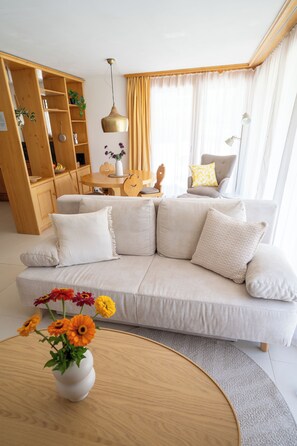 Ein modernes Wohnzimmer mit einem beige farbenen Sofa, einem Holztisch und einer Vase mit Blumen.