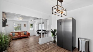 Eine moderne Küche mit einem Edelstahlkühlschrank, ein Essbereich mit weißem Tisch und Stühlen sowie ein Wohnzimmer mit einer Ledersofa.