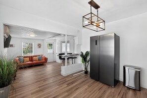Eine moderne Küche mit einem Edelstahlkühlschrank, ein Essbereich mit weißem Tisch und Stühlen sowie ein Wohnzimmer mit einer Ledersofa.