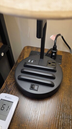 Une lampe de bureau avec une multiprise, un thermomètre numérique et une surface en bois.