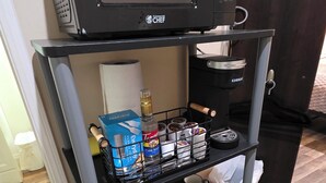 Keittiöalue, jossa on mikroaaltouuni hyllyllä, kahvinkeitin sekä erilaisia keittiötarvikkeita, kuten lautasia ja ruokailuvälineitä.