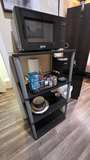 Un coin cuisine comprenant un micro-ondes posé sur une étagère, une machine à café et divers ustensiles de cuisine, comme des assiettes et des couverts.