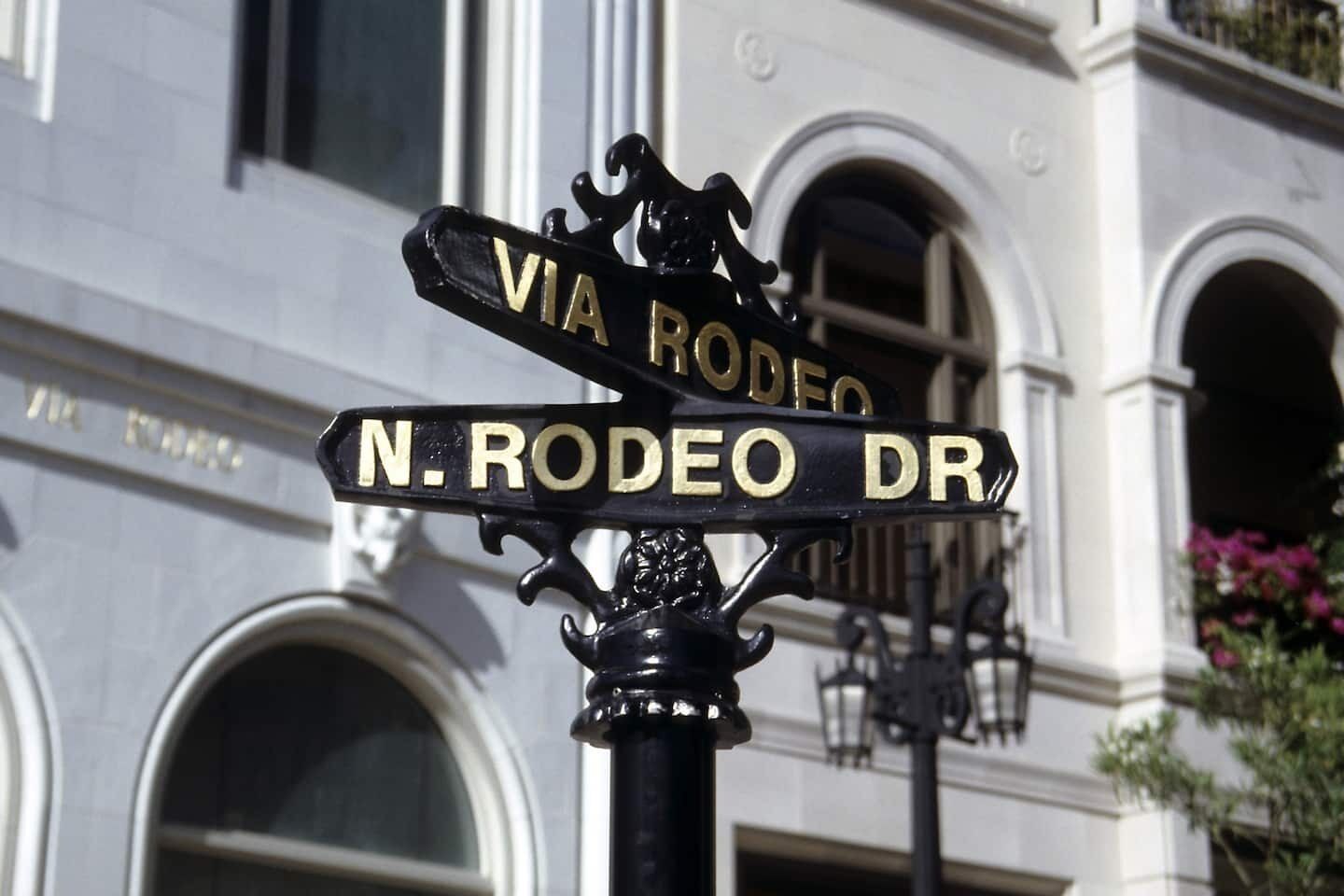 A street sign with 'VIA RODEO' and 'N. RODEO DR' indicating a street intersection.