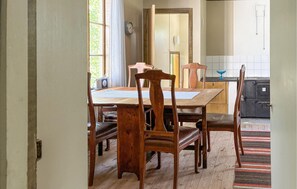 Ein Essbereich mit Holztisch und Stühlen, einem Fenster mit Vorhängen, einer Uhr und einer Küchenzeile mit Schränken und einem Spülbecken.