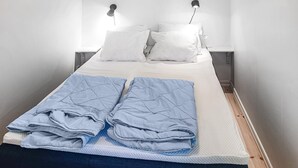 Een opgemaakt bed met witte kussens en een blauwe deken, twee nachtlampjes en een houten vloer.
