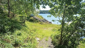 Een natuurlijk landschap met een meer, bomen en een pad dat naar een gebouw in de verte leidt.