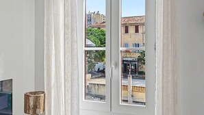 A room with a large window, white curtains, and a small table with a lamp.