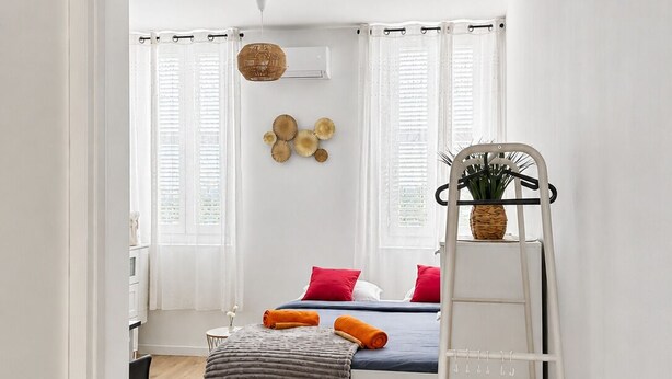 A compact bedroom with a bed, a ladder, a small table, and a window with blinds.