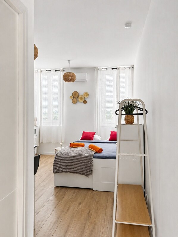 Une chambre à coucher de taille réduite, comprenant un lit, une échelle, une petite table et une fenêtre avec des stores.