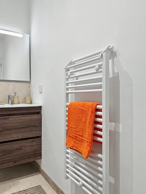 Une salle de bain avec un porte-serviettes blanc, un miroir, un meuble-lavabo en bois et un tapis beige.