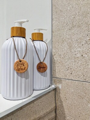 Deux bouteilles blanches, dotées de bouchons en bois et d’étiquettes, sont suspendues à une étagère blanche devant un mur à texture.