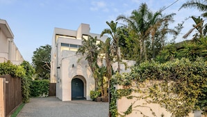 A modern building with a central arched entrance, surrounded by lush greenery and a gravel driveway. - Ultralux 5BDR Beachfront Home in Elwood (Elwood)
