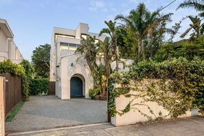 A modern building with a central arched entrance, surrounded by lush greenery and a gravel driveway. - Ultralux 5BDR Beachfront Home in Elwood (Elwood)