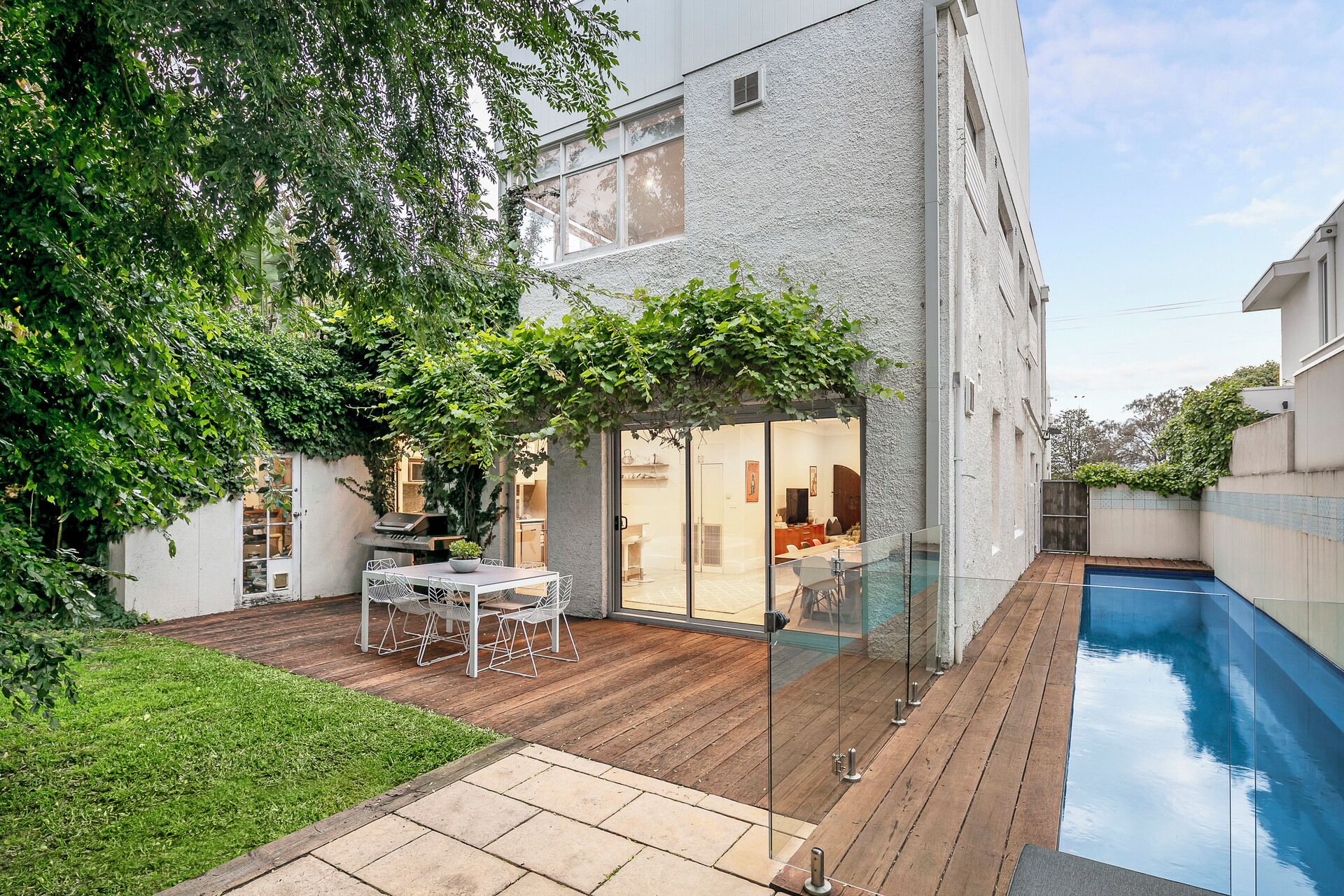 Une maison moderne dotée d’une piscine, d’un patio avec une table et des chaises, et d’une porte vitrée donnant sur un espace de vie.