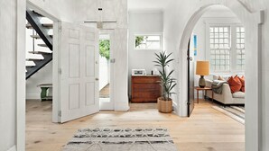 A spacious room with a staircase, a wooden cabinet, a potted plant, and a sofa with cushions. - Ultralux 5BDR Beachfront Home in Elwood (Elwood)