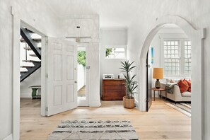 A spacious room with a staircase, a wooden cabinet, a potted plant, and a sofa with cushions. - Ultralux 5BDR Beachfront Home in Elwood (Elwood)