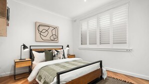 A bedroom with a bed, bedside tables, a lamp, a window with shutters, and a wall art piece. - Ultralux 5BDR Beachfront Home in Elwood (Elwood)