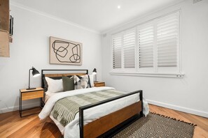 A bedroom with a bed, bedside tables, a lamp, a window with shutters, and a wall art piece. - Ultralux 5BDR Beachfront Home in Elwood (Elwood)